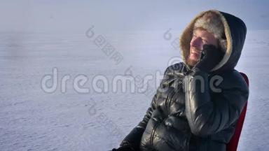 穿着保暖外套、头罩的商人在雪地里的特写肖像，在手机上愉快地交谈。